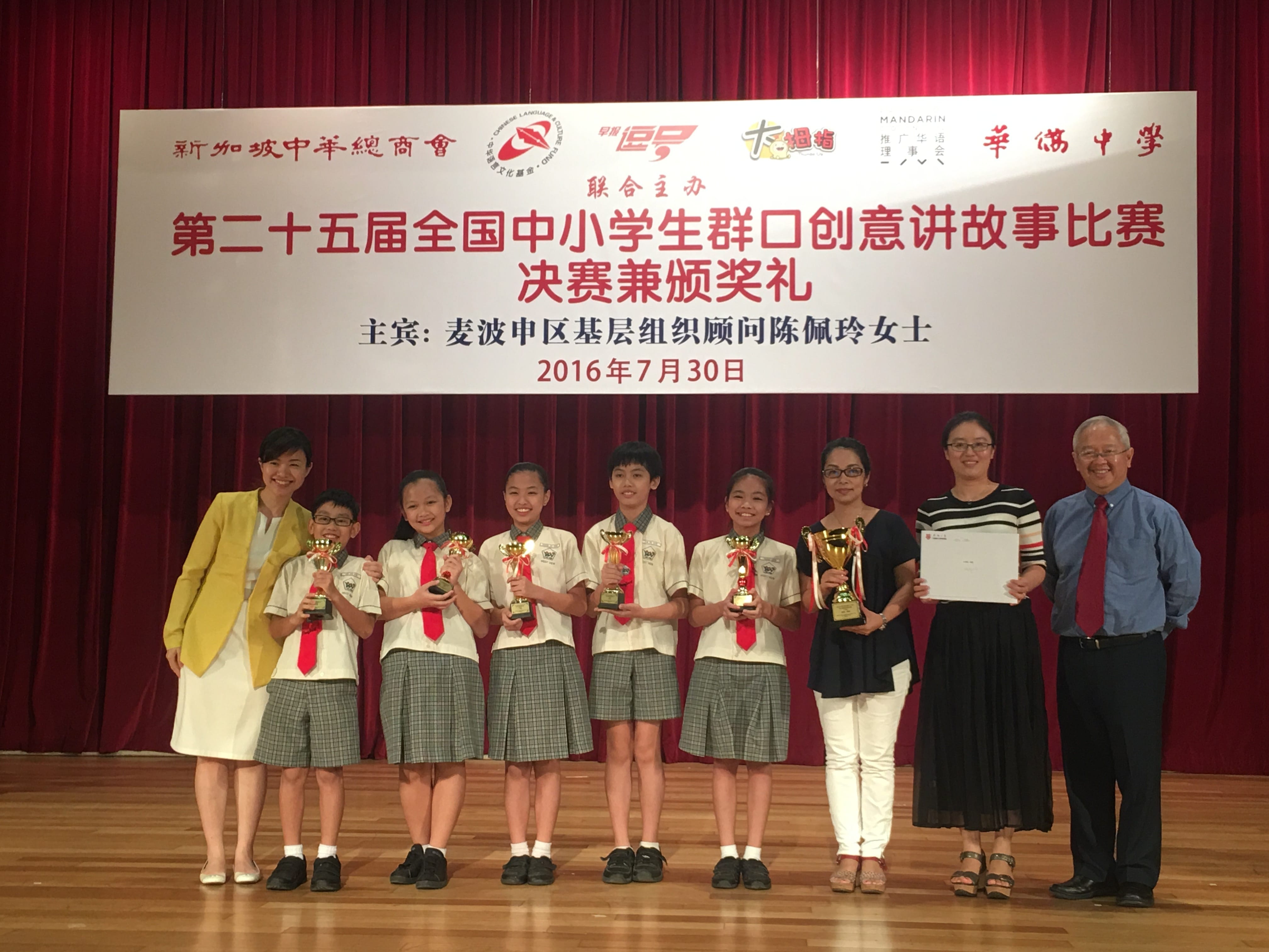 Students in school uniforms hold trophies on a stage with a Chinese banner at an awards ceremony dated July 30, 2016.